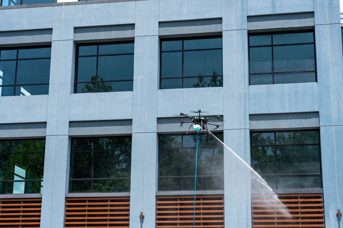 Sherpa cleaning drone spraying the glass exterior of a blue commercial office building