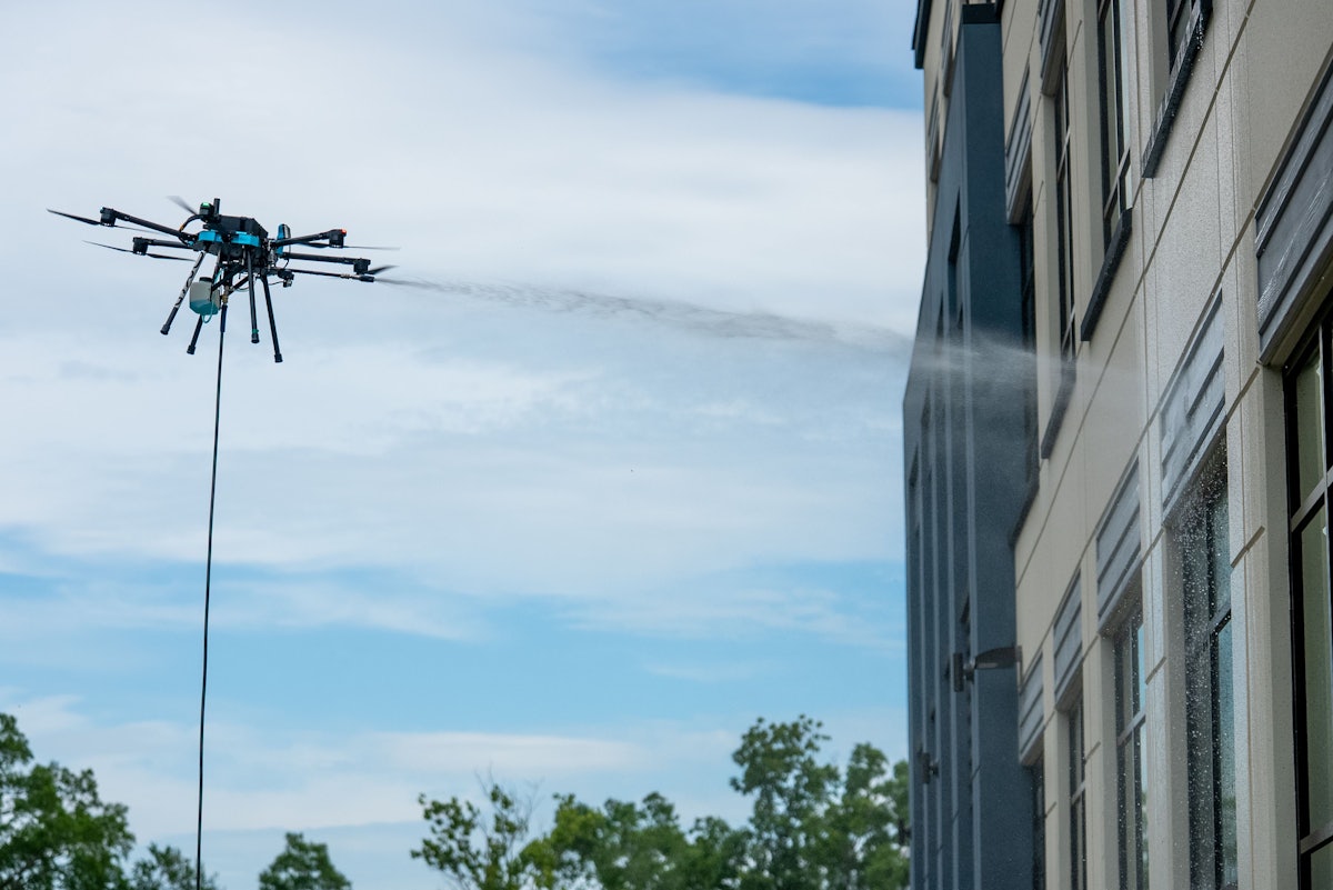 Drone spraying water on the exterior of a tall industrial building